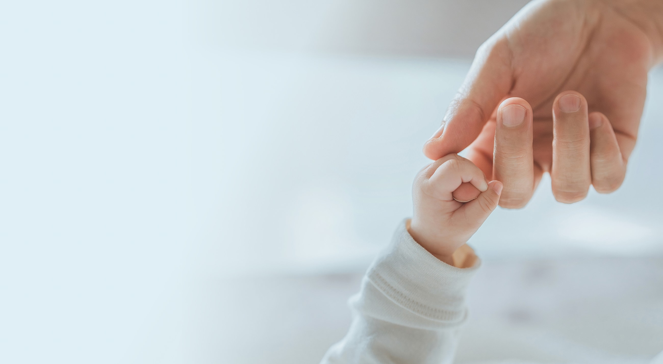 Adult hand gently holding baby's hand.