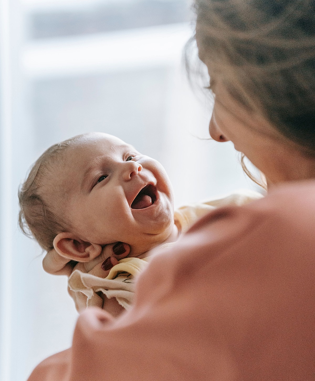 Happy baby smiling at mother in soft light.