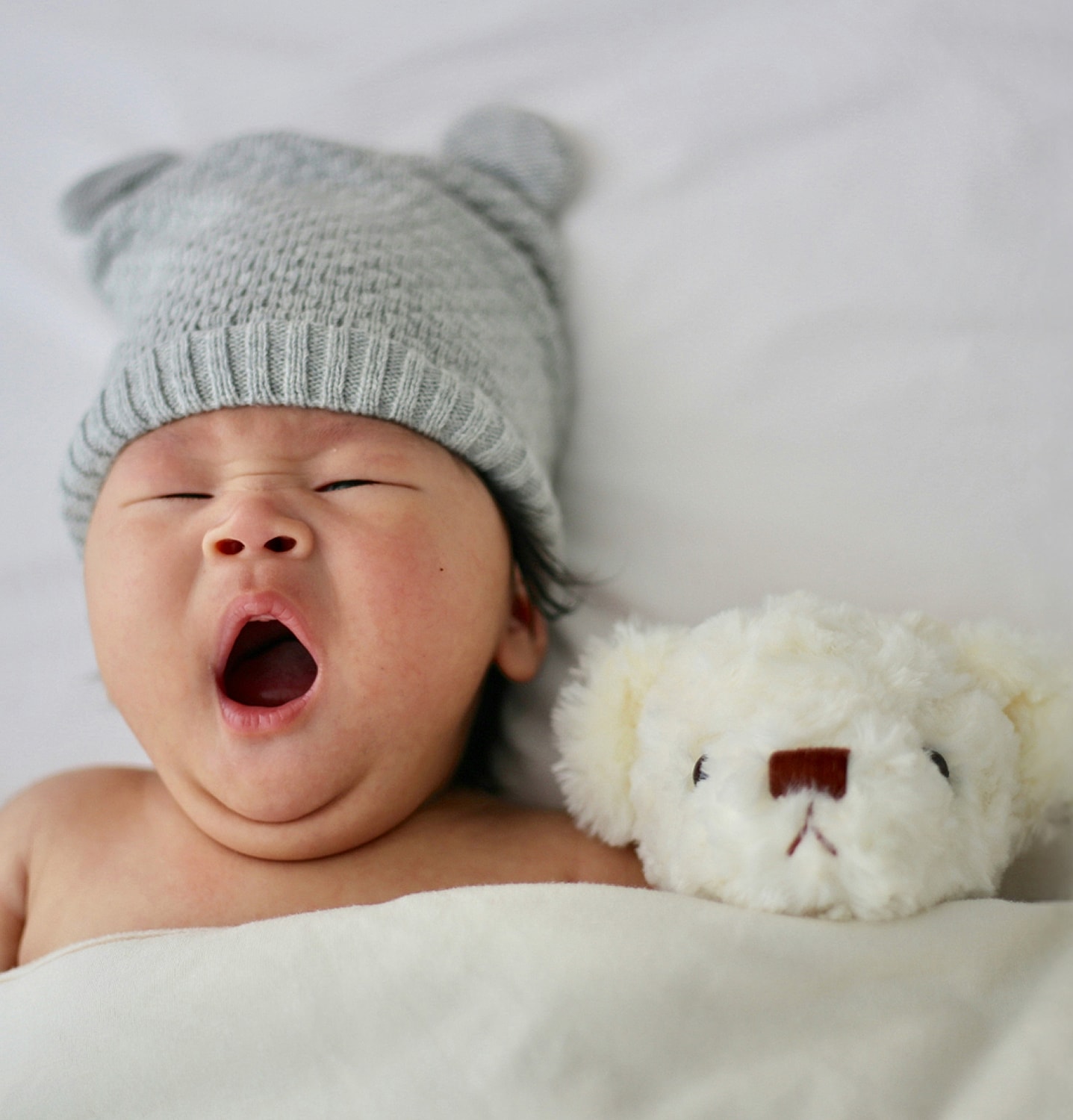 Baby yawning with stuffed animal companion.