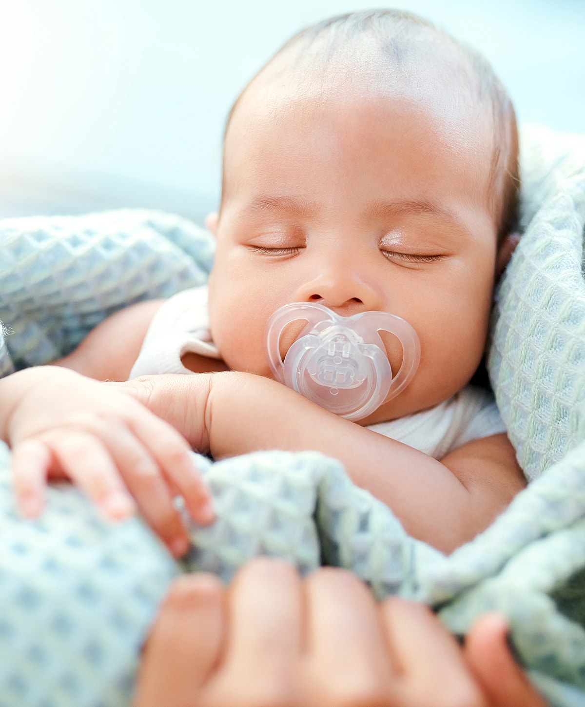 Sleeping baby with pacifier wrapped in blanket.