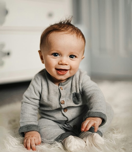 Smiling baby sitting on soft carpet.