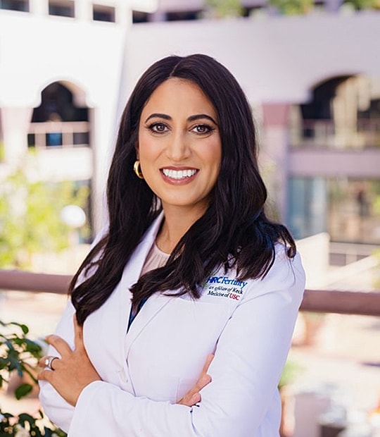 Smiling woman in white lab coat outdoors.
