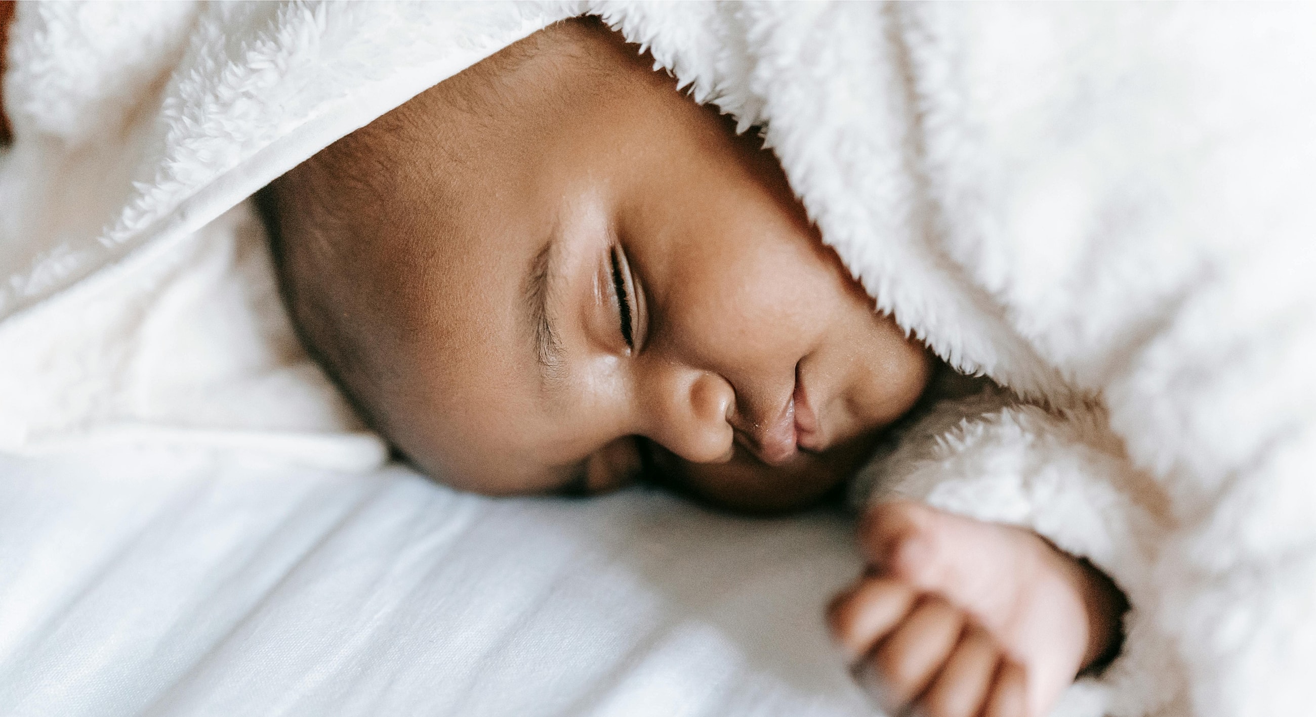 Sleeping baby wrapped in soft white blanket.