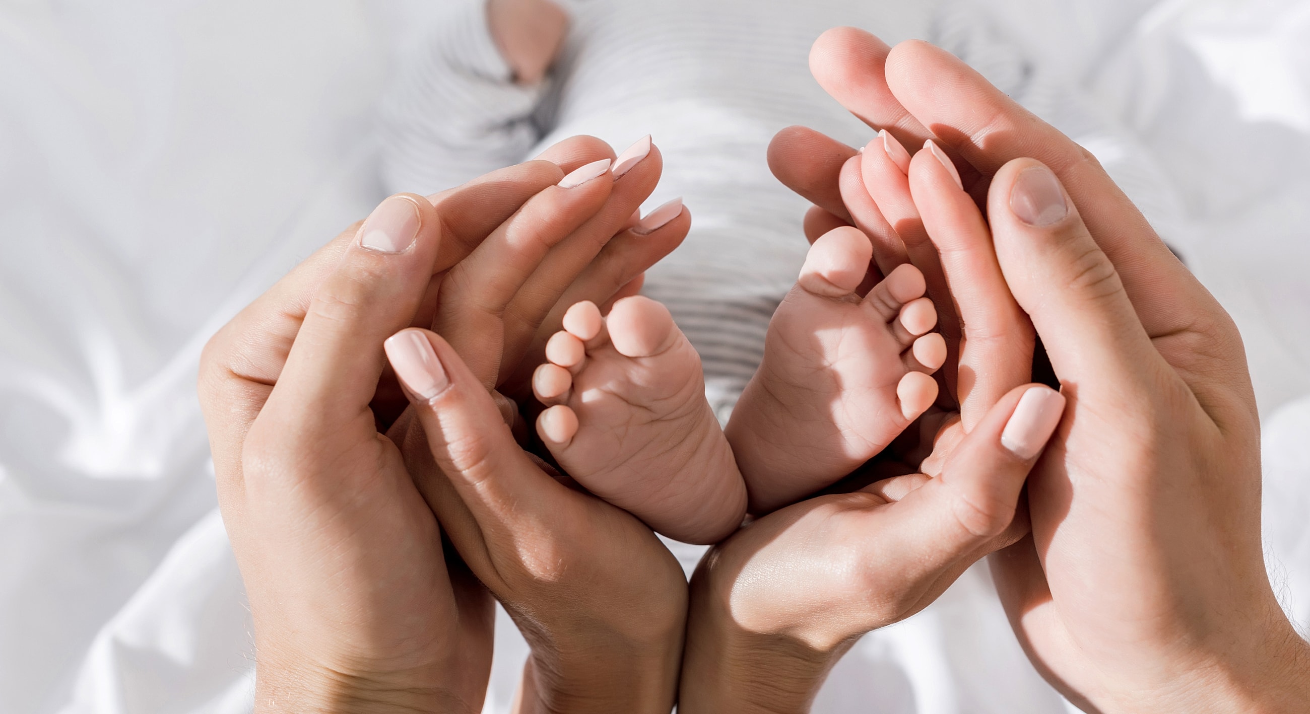 Hands cradling a baby's feet on soft fabric.
