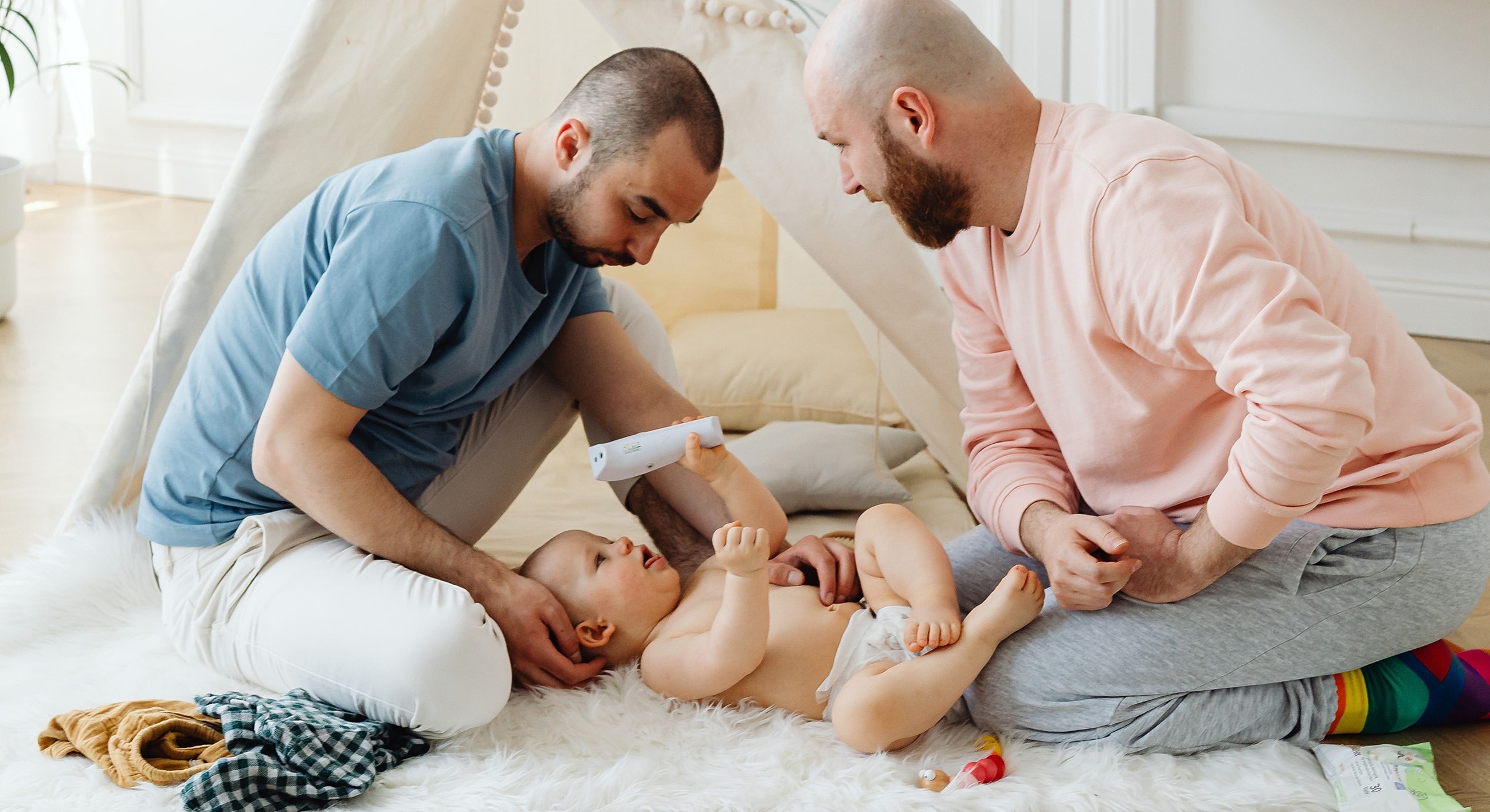 Two men caring for a baby on the floor.