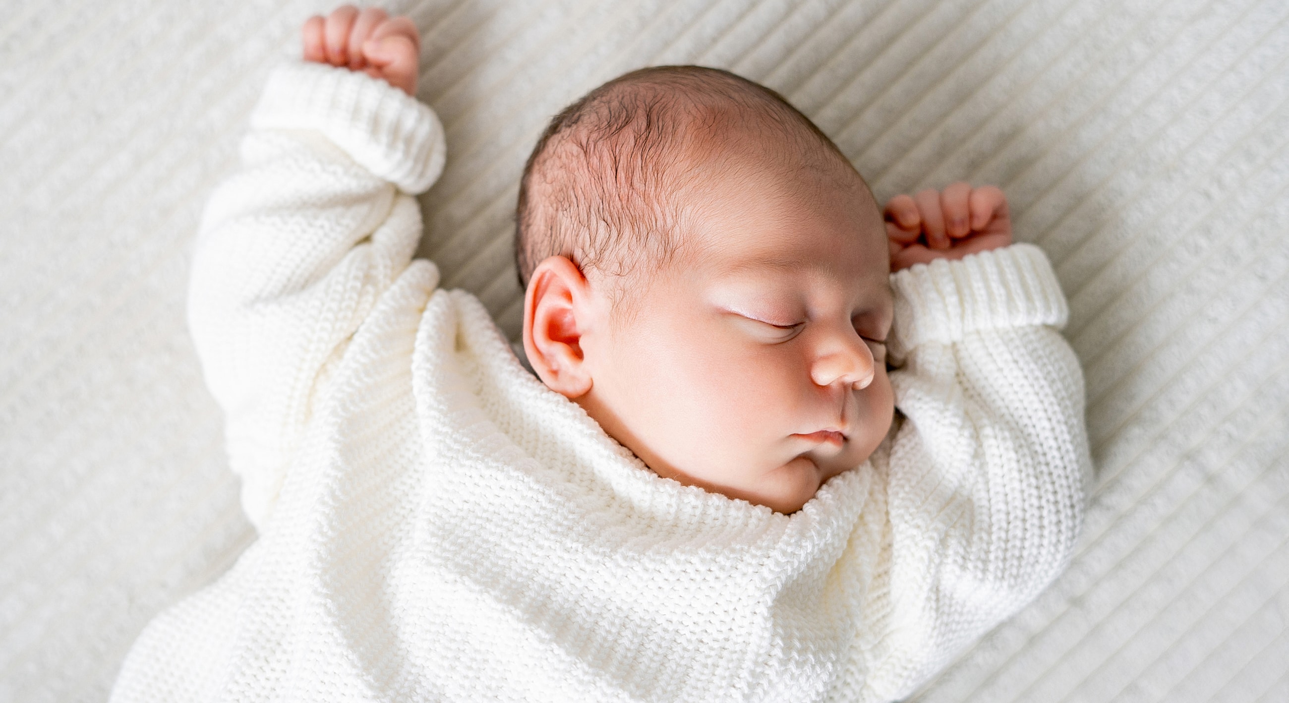Sleeping baby in a cozy white sweater.
