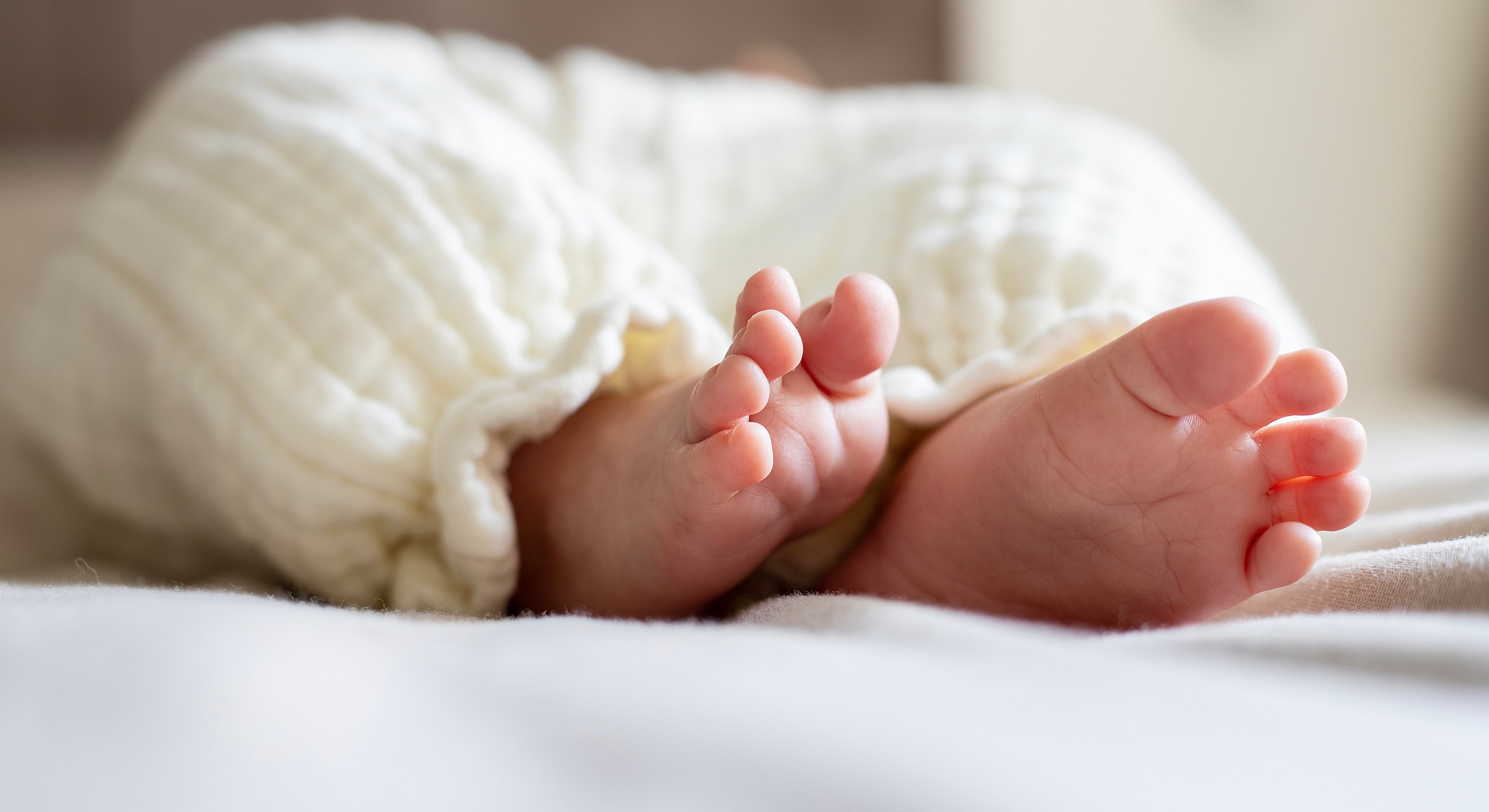 Baby feet in soft white blanket on bed.
