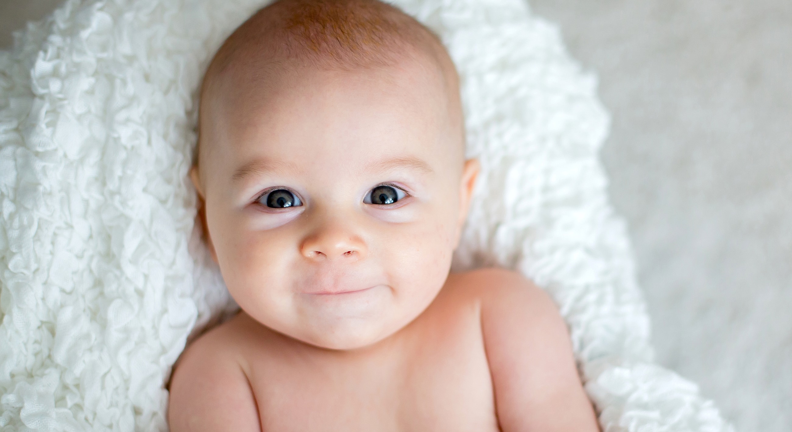 Smiling baby on a white blanket.