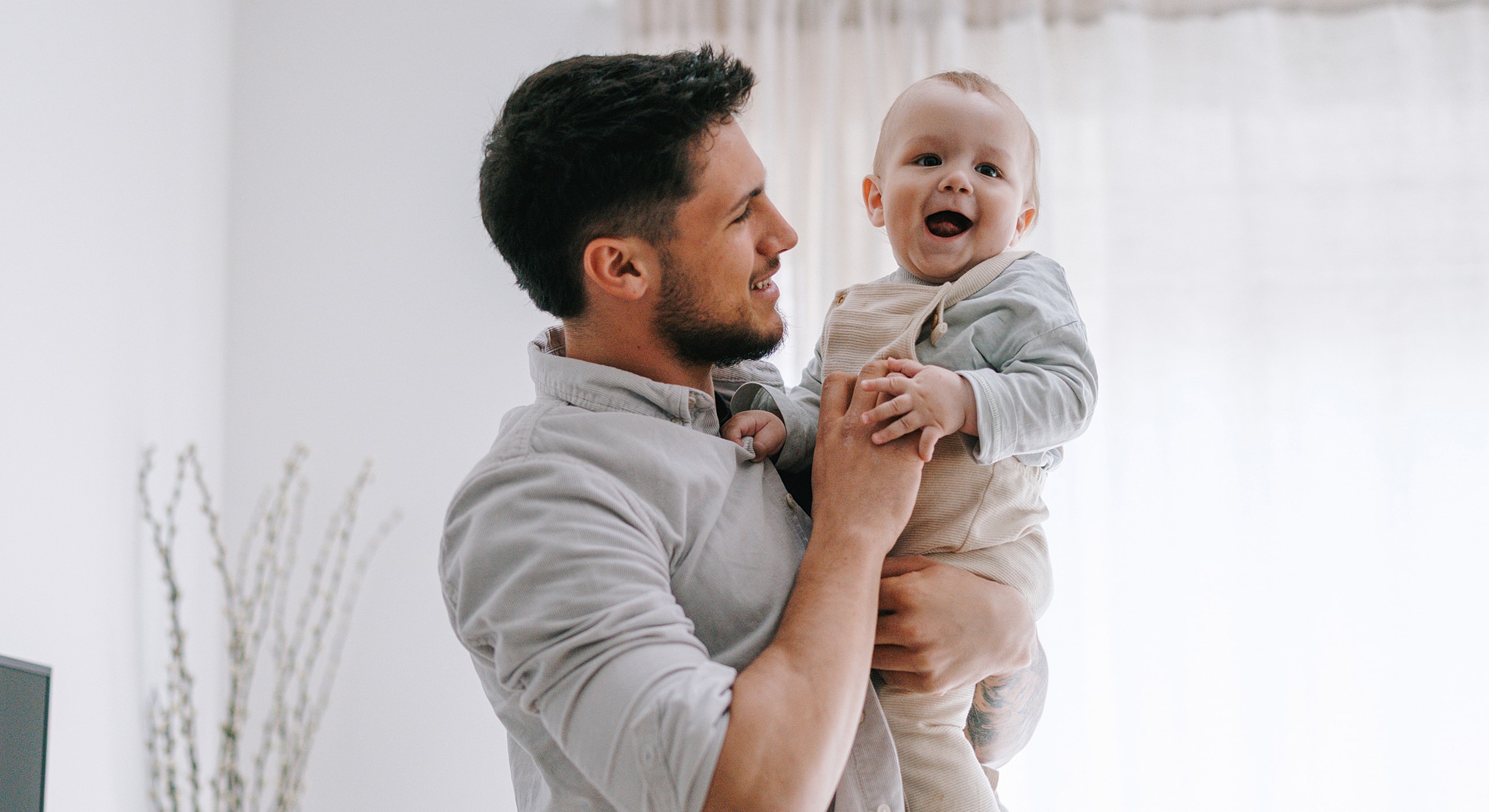 Father joyfully holding smiling baby indoors.