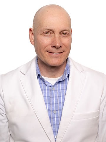 Smiling man in a white coat, professional attire.