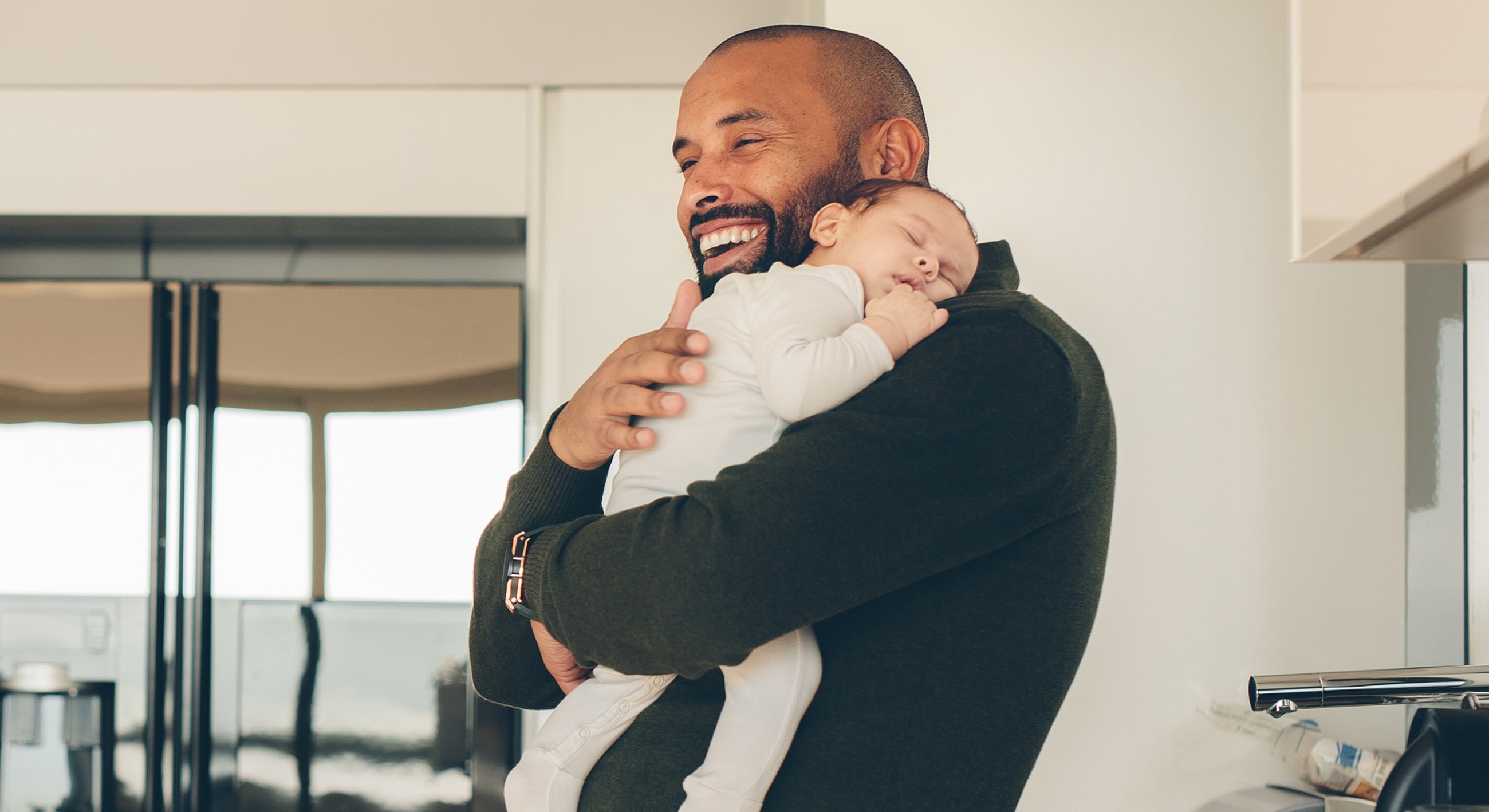 Smiling father holding sleeping baby indoors.